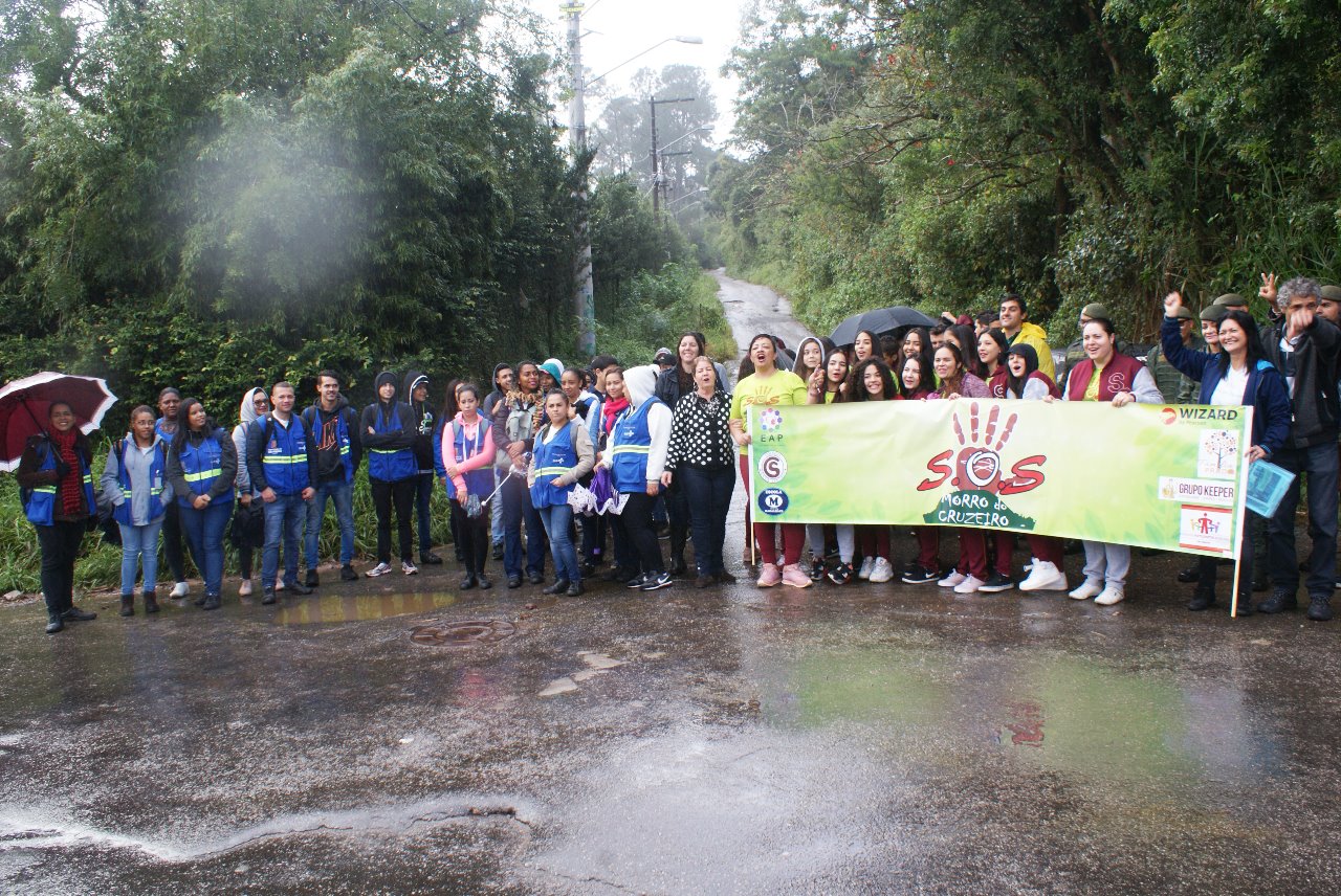 Participantes da caminhada em frente ao Morro do Cruzeiro; à direita, seguram uma faixa com uma mensagem da causa ecológica.